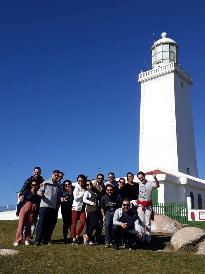 Rodney com um grupo de cerca de quinze pessoas diante de um farol branco